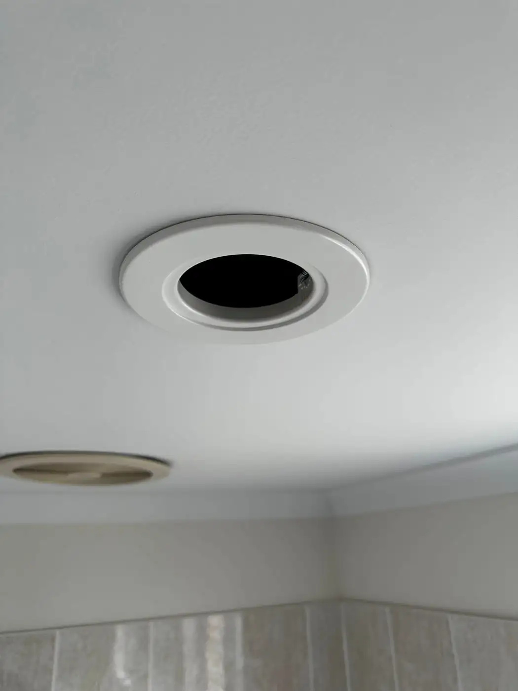 The new white LED trim installed in the same ceiling opening, a second old can still visible behind it