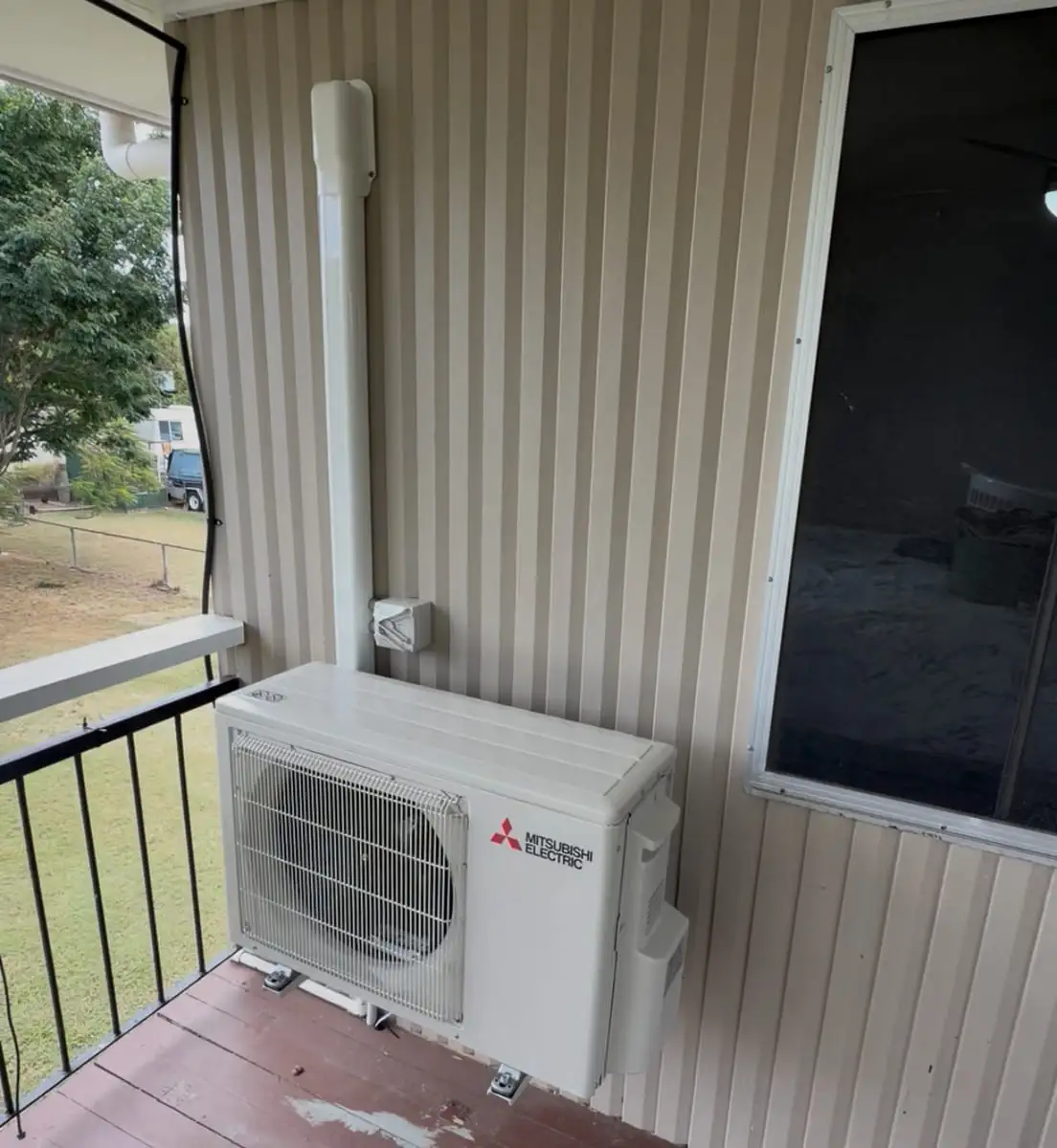 A new Mitsubishi Electric outdoor unit installed on feet on a timber deck against a cream clad wall