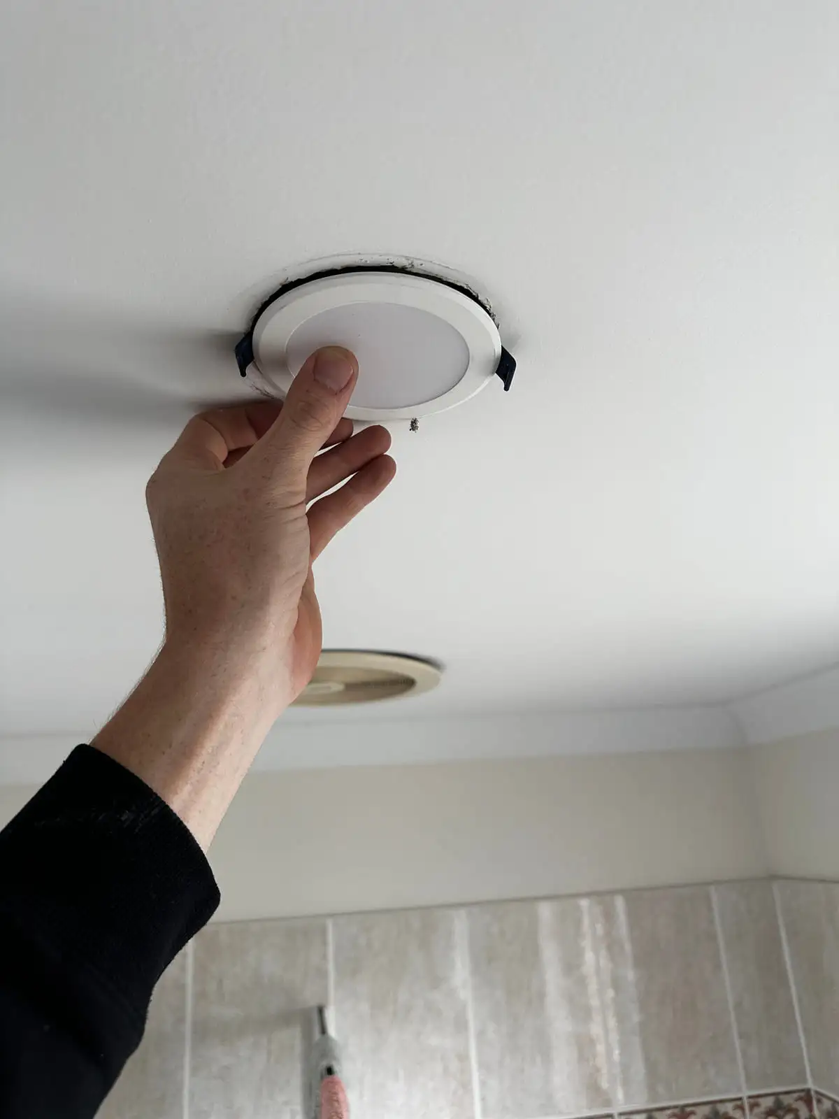 An electrician's hand clipping a new white LED downlight up into a ceiling opening
