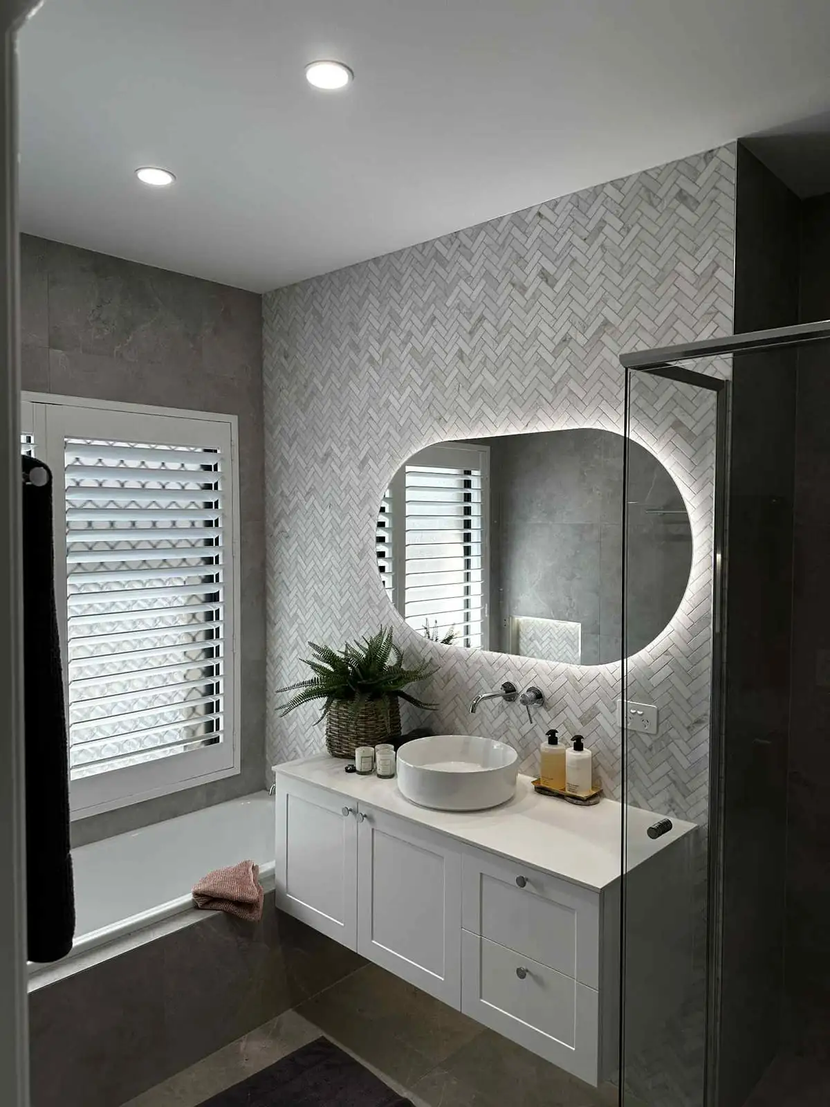 A finished renovated bathroom with a backlit round mirror and downlights over the vanity