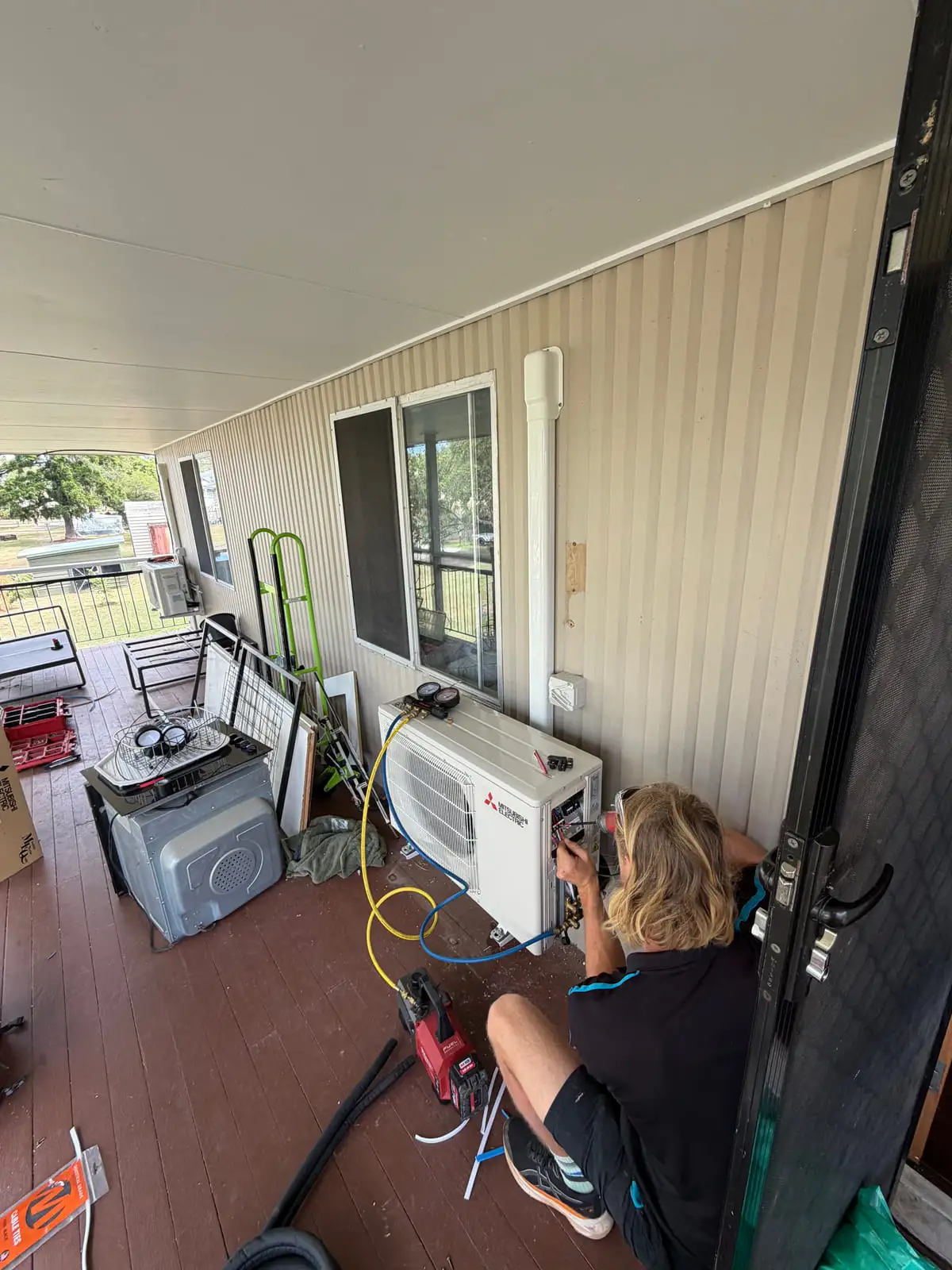 The old outdoor unit off to one side on a deck while the new Mitsubishi Electric one is connected