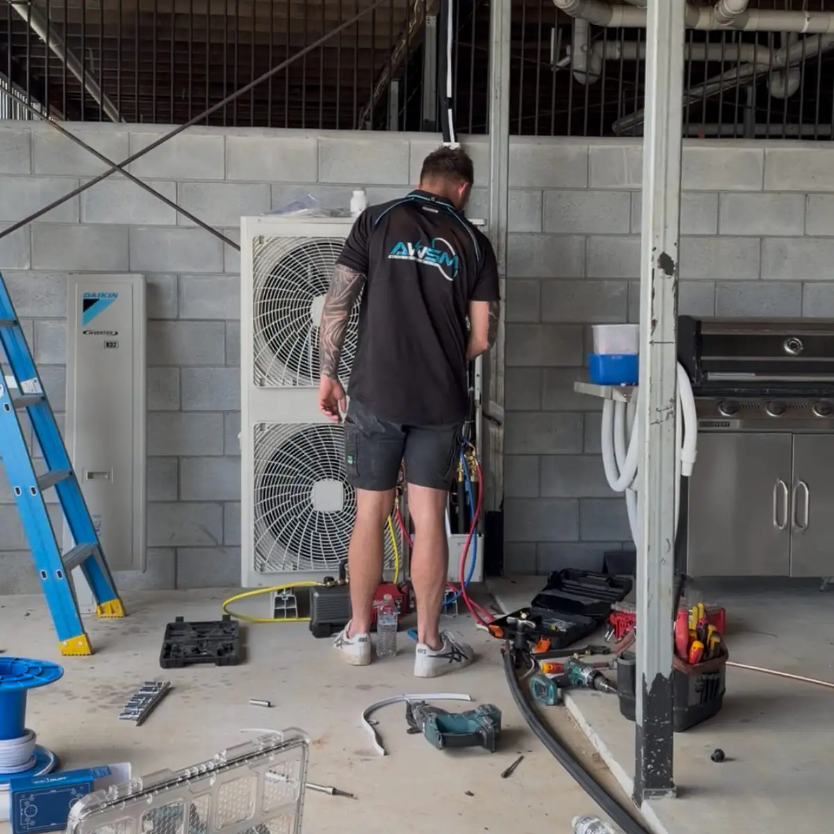 An AWSM installer connecting two Daikin outdoor units stacked on brackets under a carport