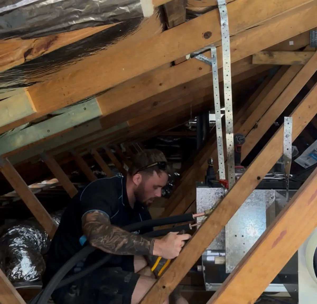 An AWSM installer in a roof space running flexible duct to a plenum between the rafters