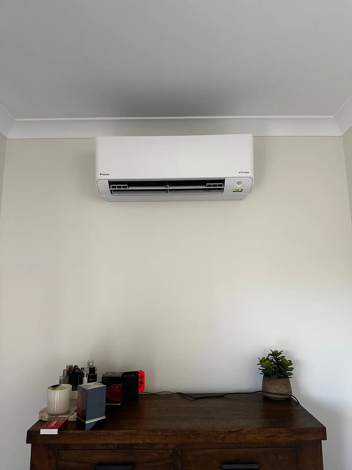 A Daikin split system head unit installed high on a clean wall above a living room sideboard