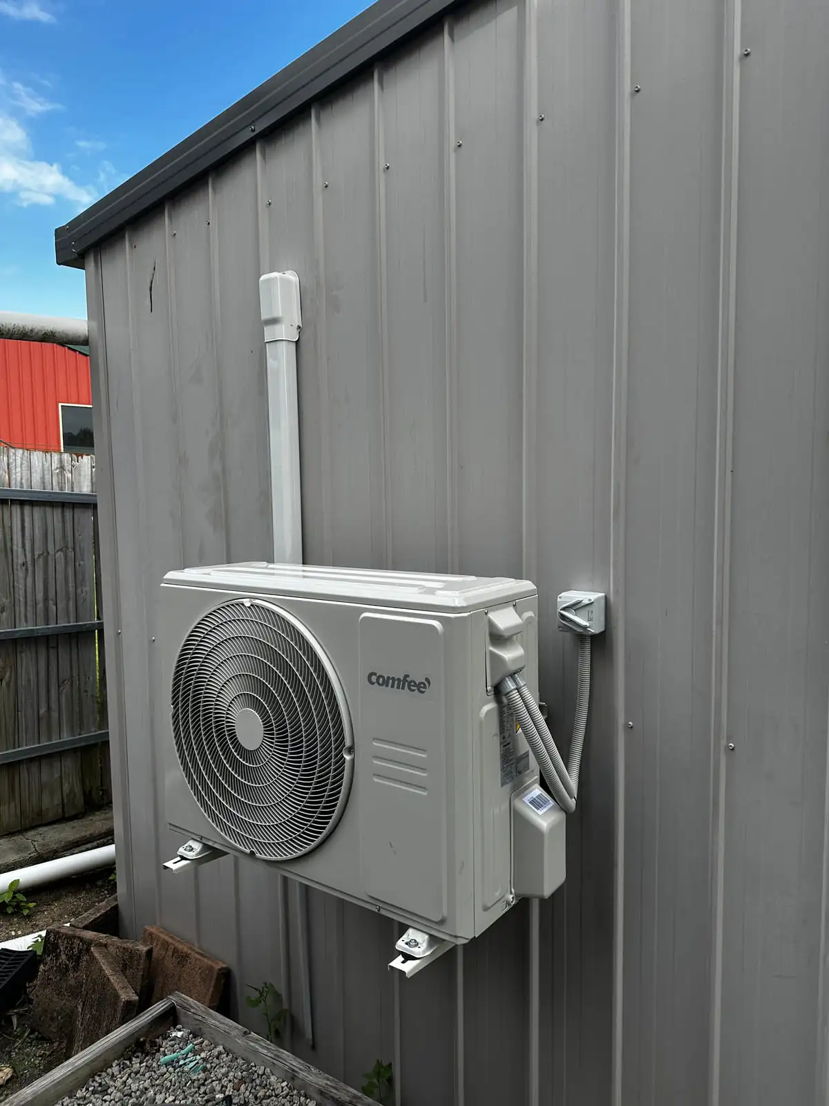 The matching outdoor unit bracketed to the outside of the shed wall with an isolator beside it