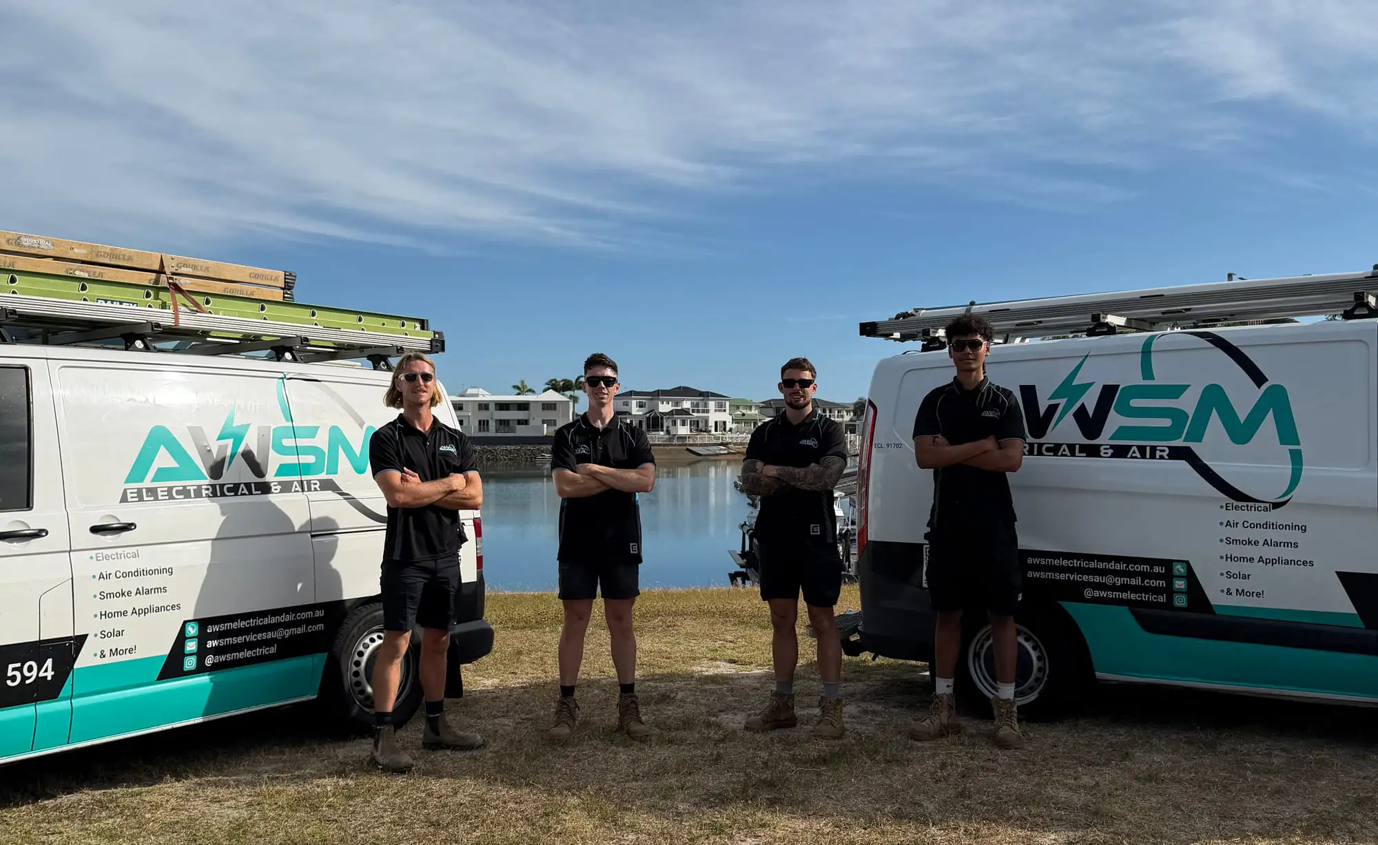 The four of the AWSM crew standing between their two signwritten vans beside the water